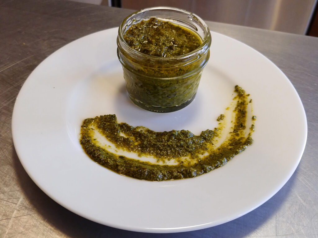 Pesto Recipe: Pesto in a small jar, on the white plate, all on the table, side view