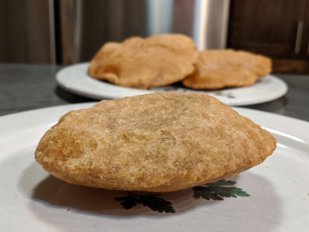 one Poori Bread in front on the plate, on other plate behind two other poori breads