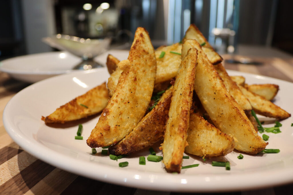 Oven-Roasted Potato Wedges plied on the plate with sauce and kitchen in the background, close up shot - example of Sides and Sauces