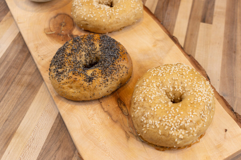 Bagels baked accoriding my Bagel Recipe on the rustic wooden cutting board. Close up to 3 bagels from top side.
