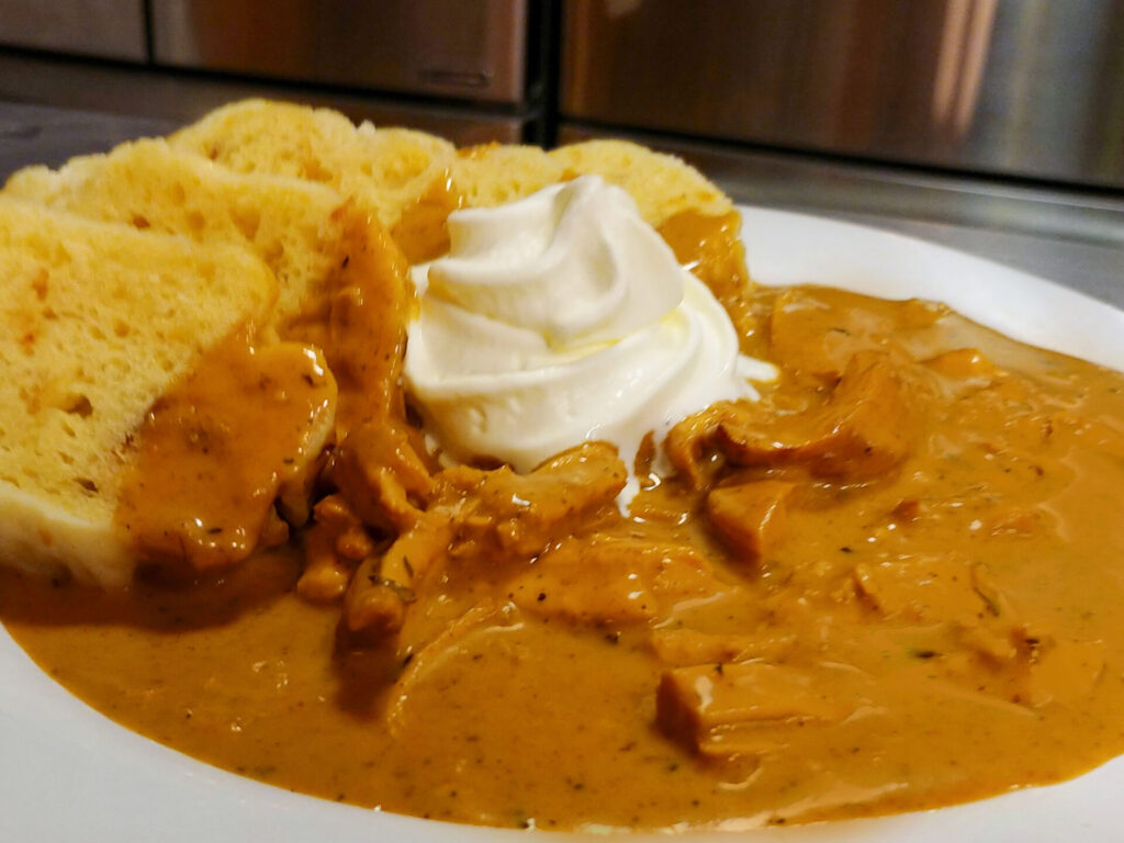 Creamy Paprika Chicken Kuře na Paprice on the white plate on the table with refrigerators behind. Close up shot