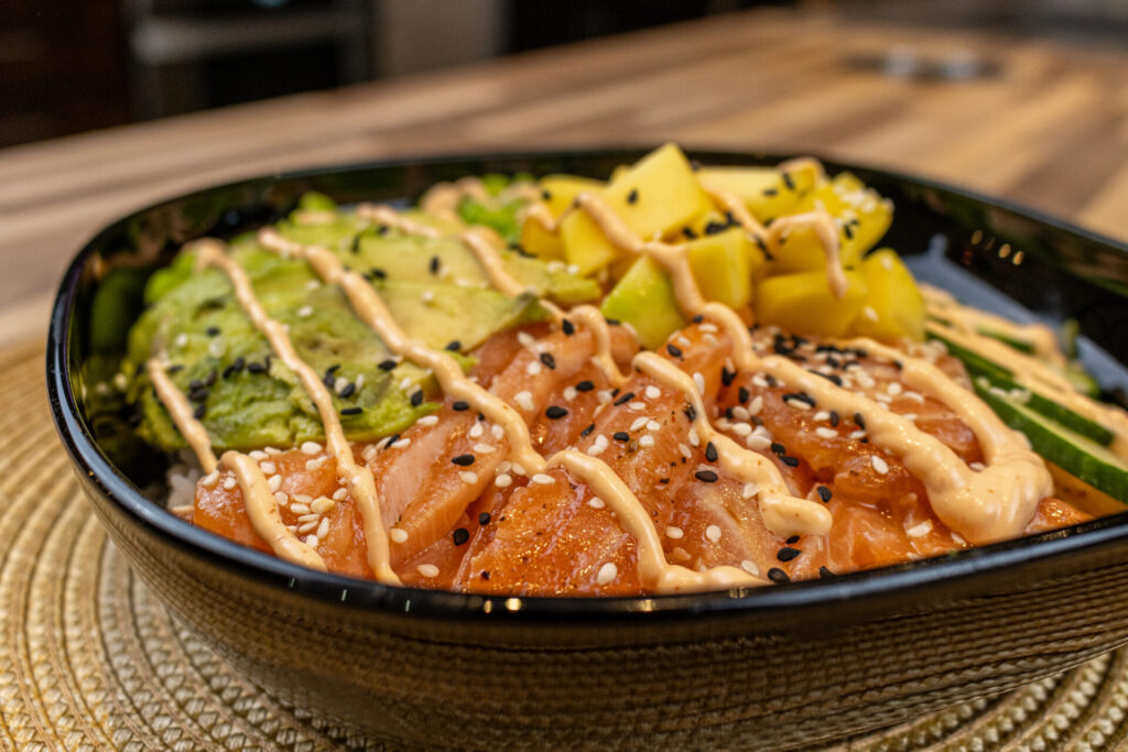 Poke Bowl with Salmon in the black bowl, on the countertop with part of the kitchen in background