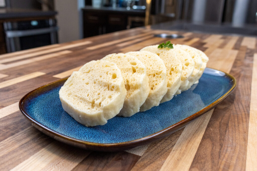 Czech Bread Dumpling Houskovy Knedlik Recipe on the blue plate with kitchen in the background, medium close up shot