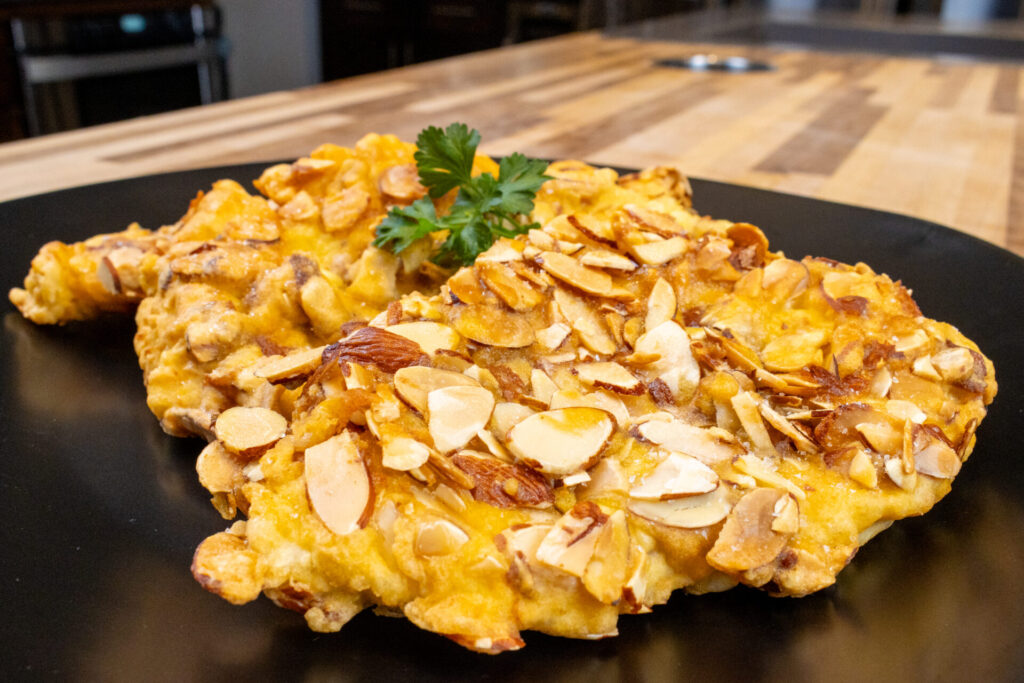 Almond Chicken Schnitzel on the black plate, side shot, kitchen in background