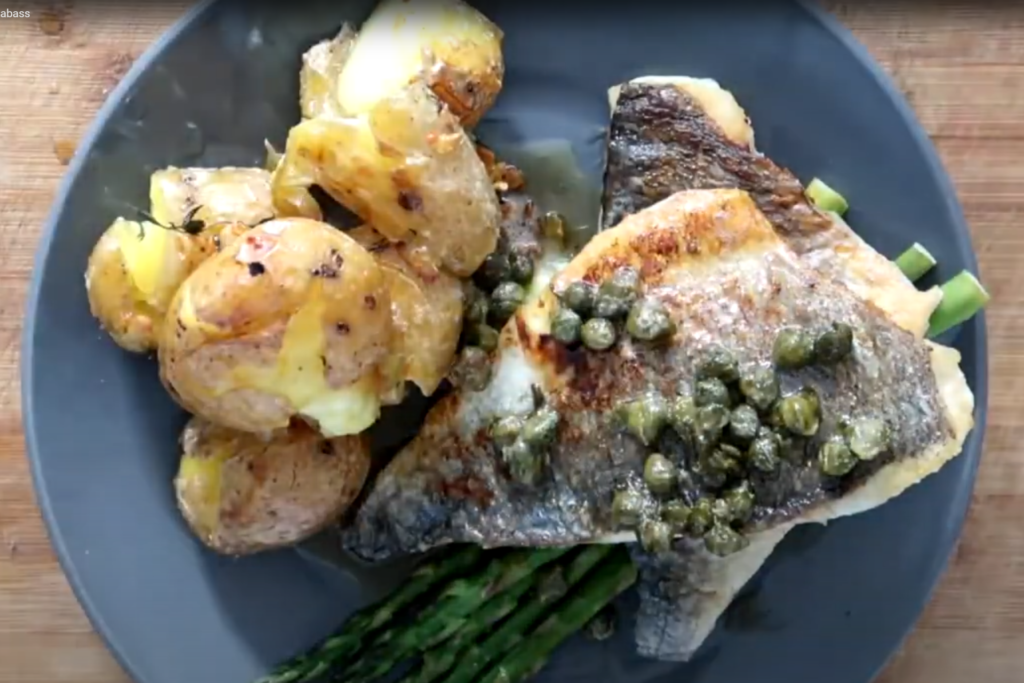Pan-Fried Sea Bass with Crushed Potatoes and Asparagus on the dark plate, top view