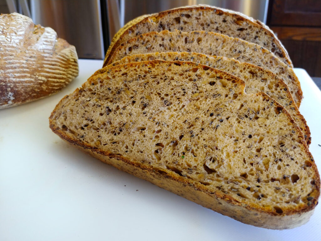 Sliced Multigrain Bread on the white cutting board, with the entire loaf in the background.