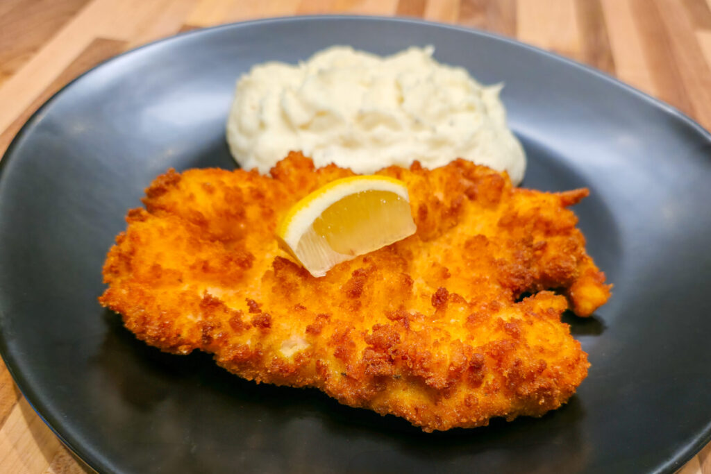 Cheese Battered Chicken Schnitzel Kuře v Sýrovem Těstíčku on the black plate, close up side shot 2