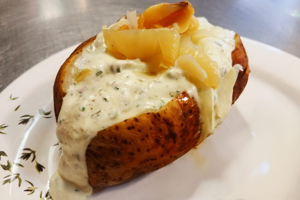 Baked Potato with Herb Sour Cream on the plate, with sauted onion, detail shot