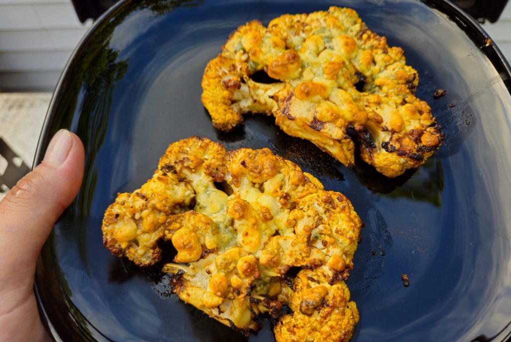 Buffalo Cauliflower Steak on the black plate, in hands, close up shot