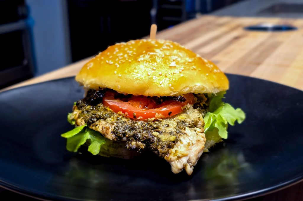 Pesto Chicken Sandwich with Parmesan on the black plate, close up side shot with the kitchen in the background
