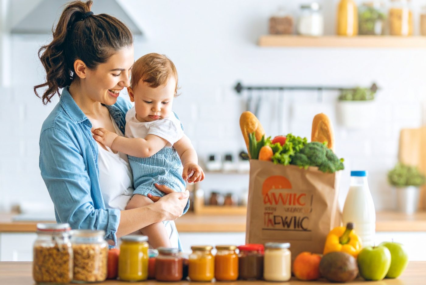 smiling mother holding her infant while a slightly older toddler points to healthy items