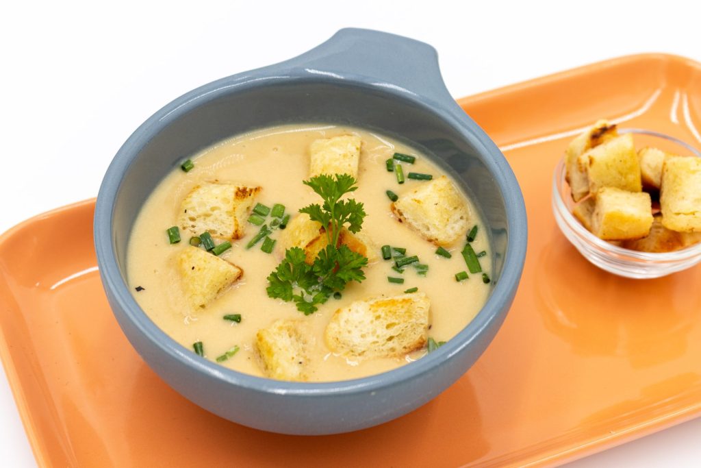 Czech Garlic Soup Cesnecka in the gray bowl on the orange tray with crotons on the side as well as with extra croutons on the side. Isolated on the white background. Colose up side top shot