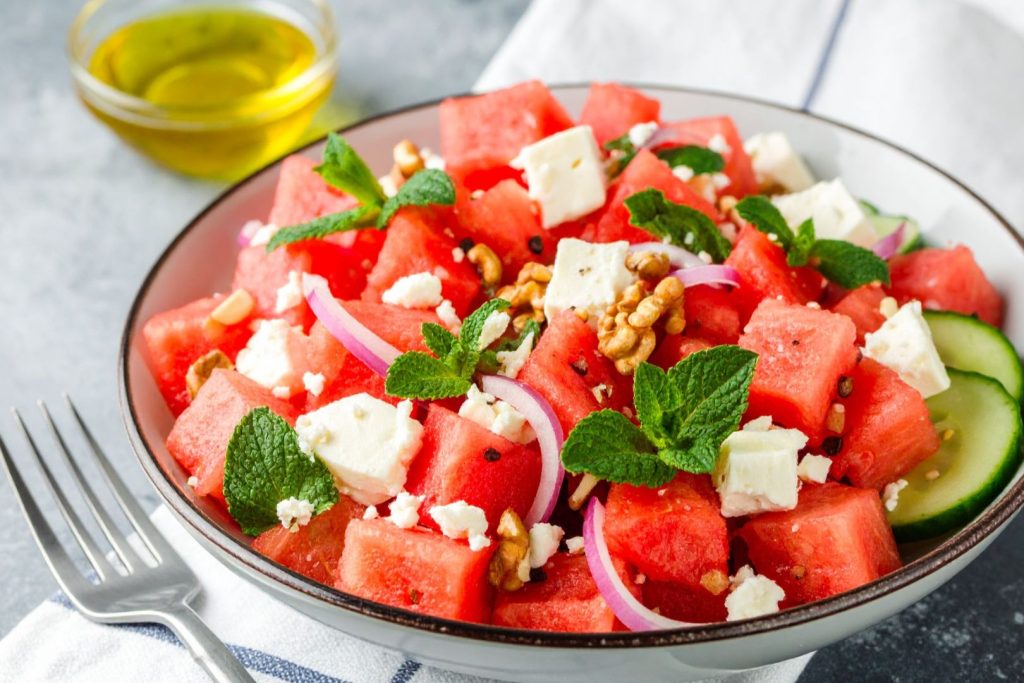 Watermelon and Feta Salad on the plate on the table with fork and extra oil next to it, close up shot
