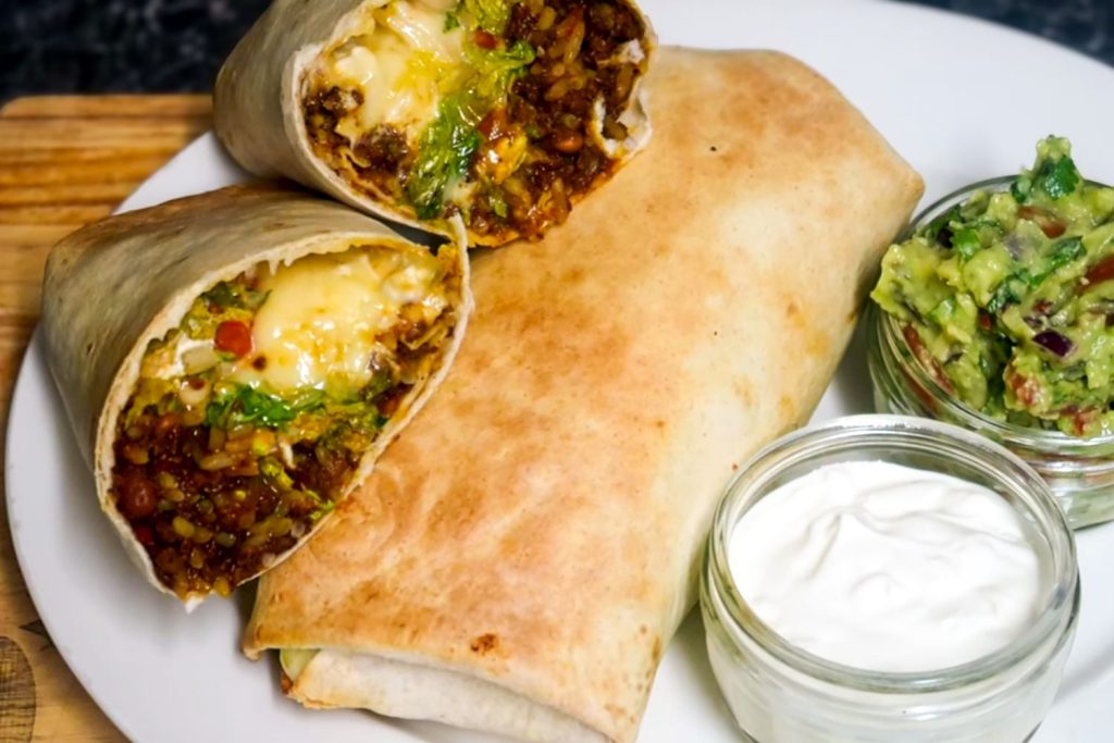 The Ultimate Chili Burritos with sour cream and quacamole on the white plate