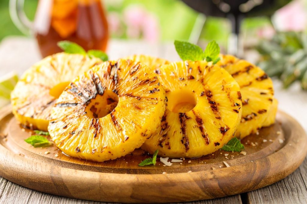 Grilled Pineapple on the cutting board with ice tea and grill in the background, close up shot