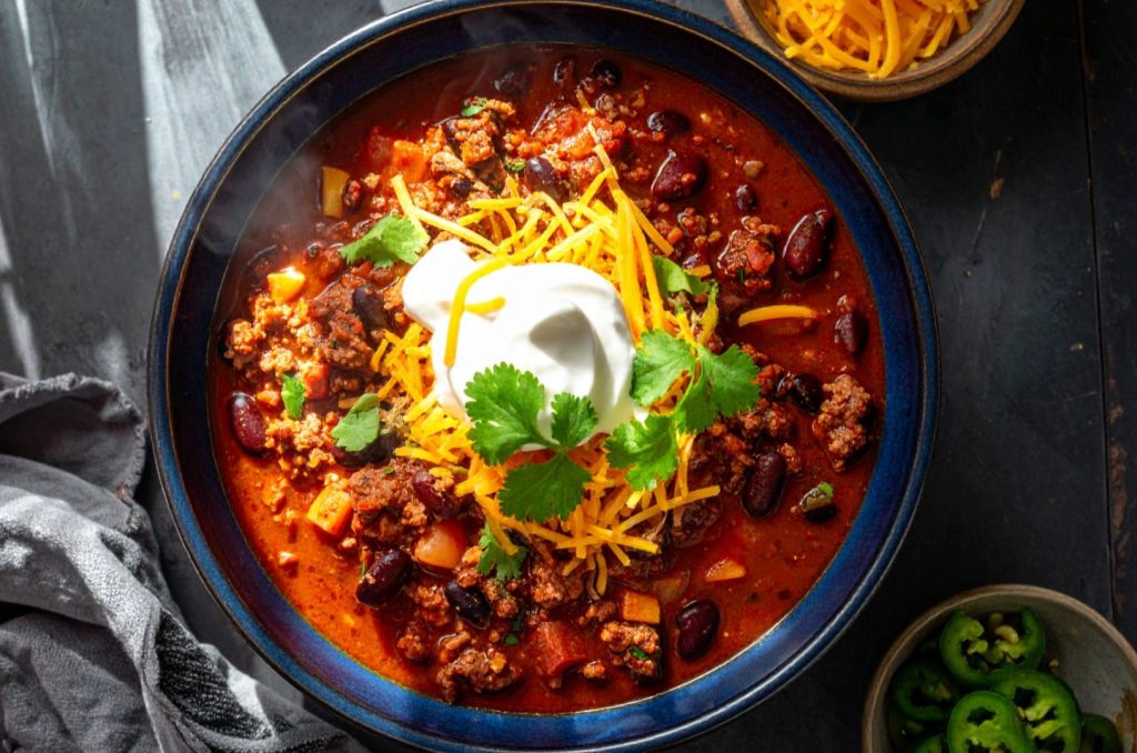 top shot of delicious and freshly cooked chili in the bowl, topped with shredded chees, sour cream and fresh cilantro